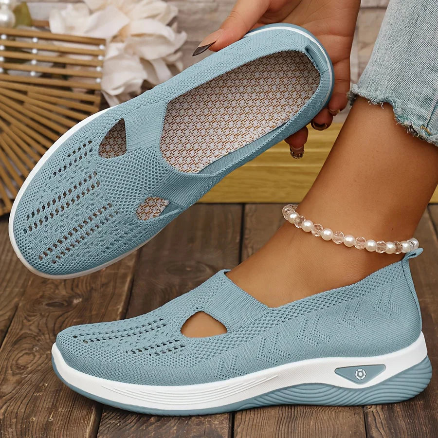 Blue slip-on shoes with white soles worn by a person on a wooden floor.