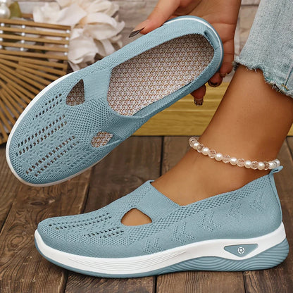Blue slip-on shoes with white soles worn by a person on a wooden floor.